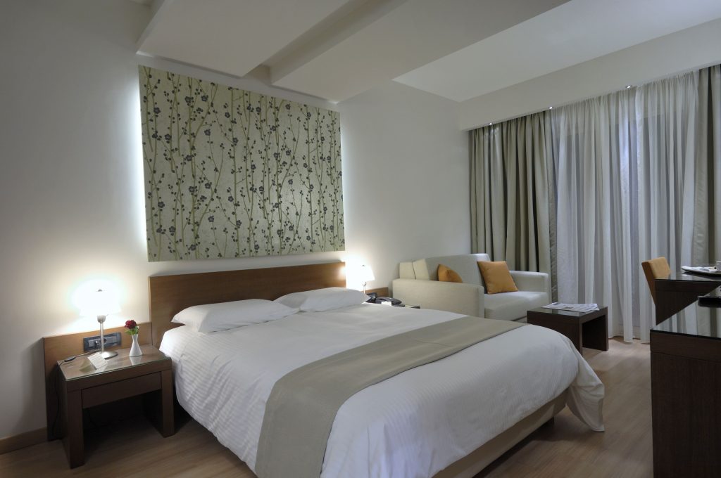 Relax in comfort with a large bed, nightstand, and chair, surrounded by a modern design and natural light.